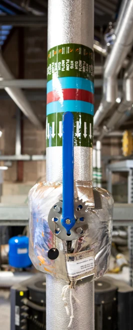 Close-up of an insulated pipe with a blue control valve and directional labeling in a building services training environment. Close-up of an insulated pipe with a blue control valve and directional labeling in a building services training environment.